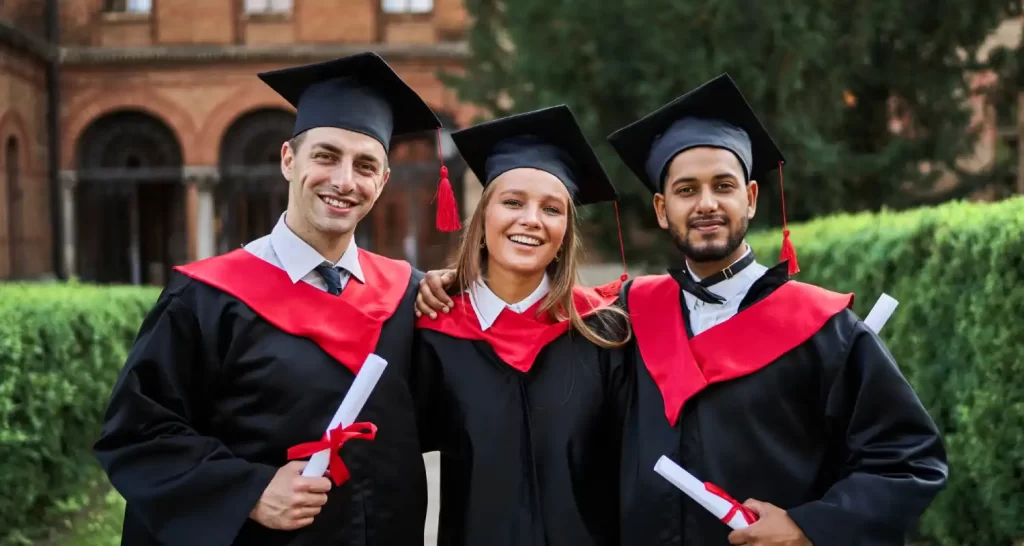 Portrait of three smiling graduate friends in graduation robes in university campus with diploma.