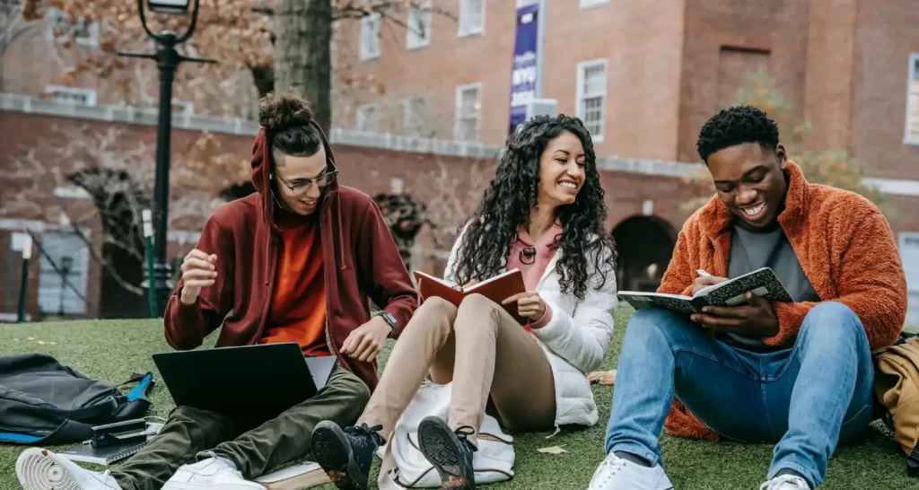 Cheerful multiethnic students with books sitting near university
