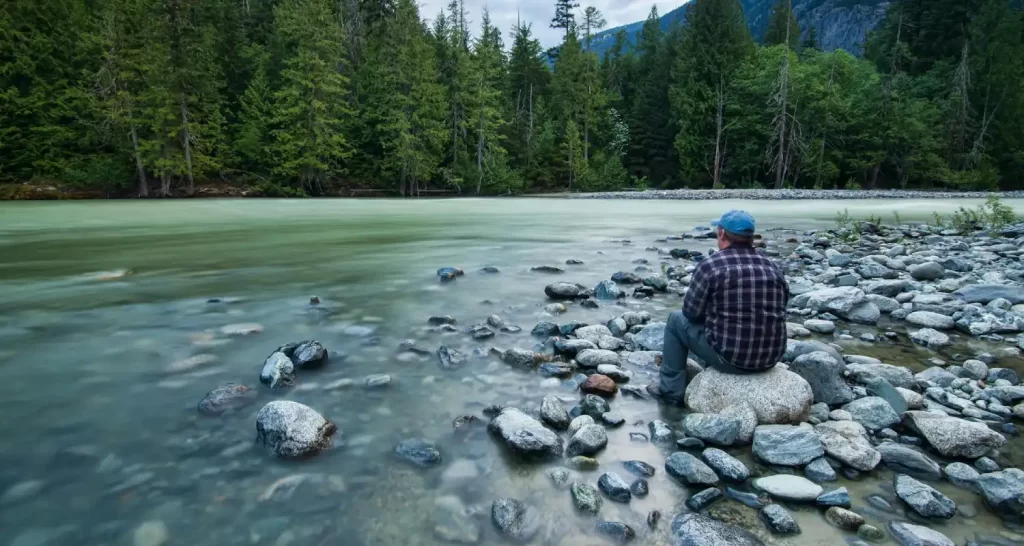 Person Sitting on Stone Near Body of Water