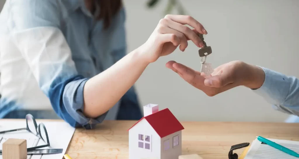 Close-up of woman's hand giving house key to man over wooden table
