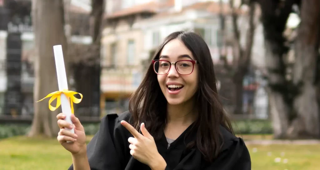 Young woman at graduation ceremony pointing to her diploma