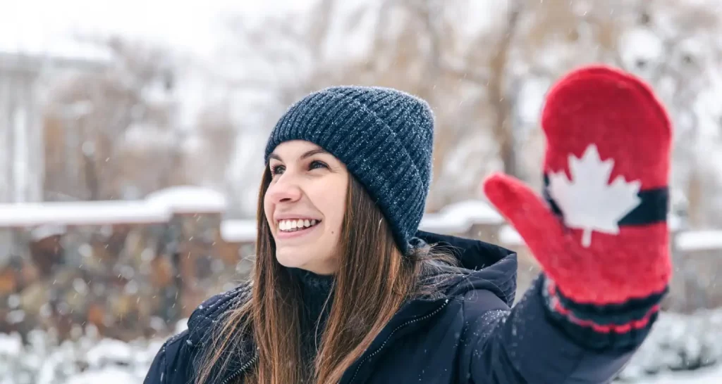 Happy young woman in red mittens with the flag of canada in snowy weather