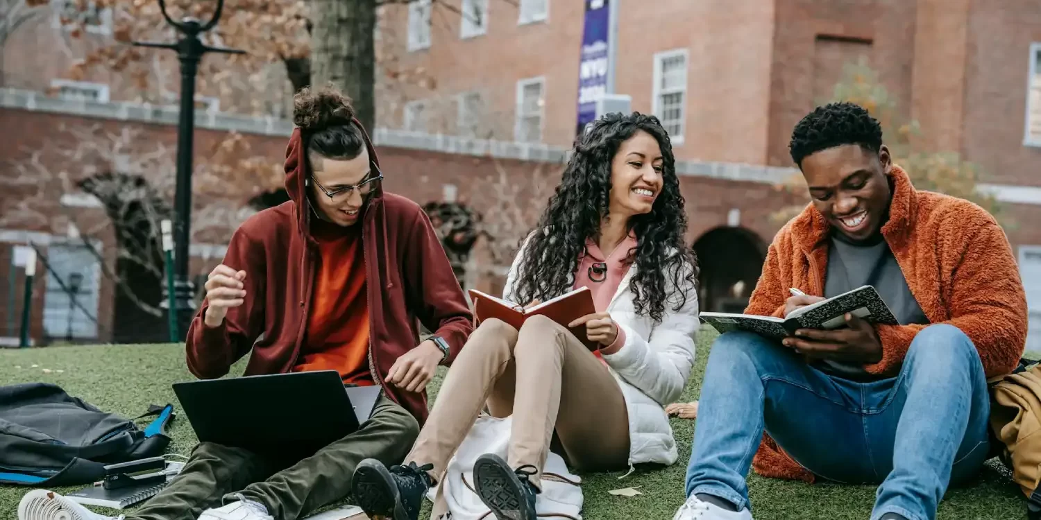 Cheerful multiethnic students with books sitting near university