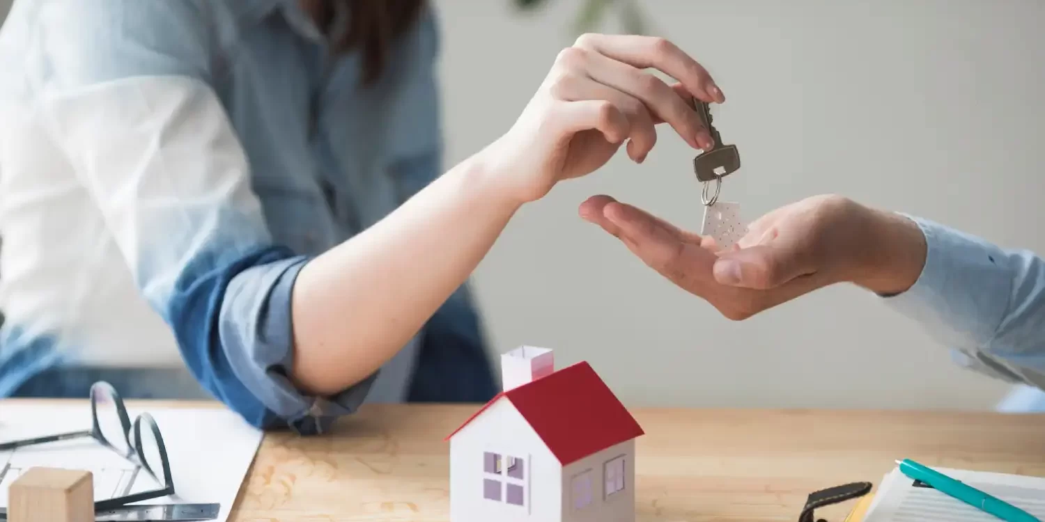 Close-up of woman's hand giving house key to man over wooden table