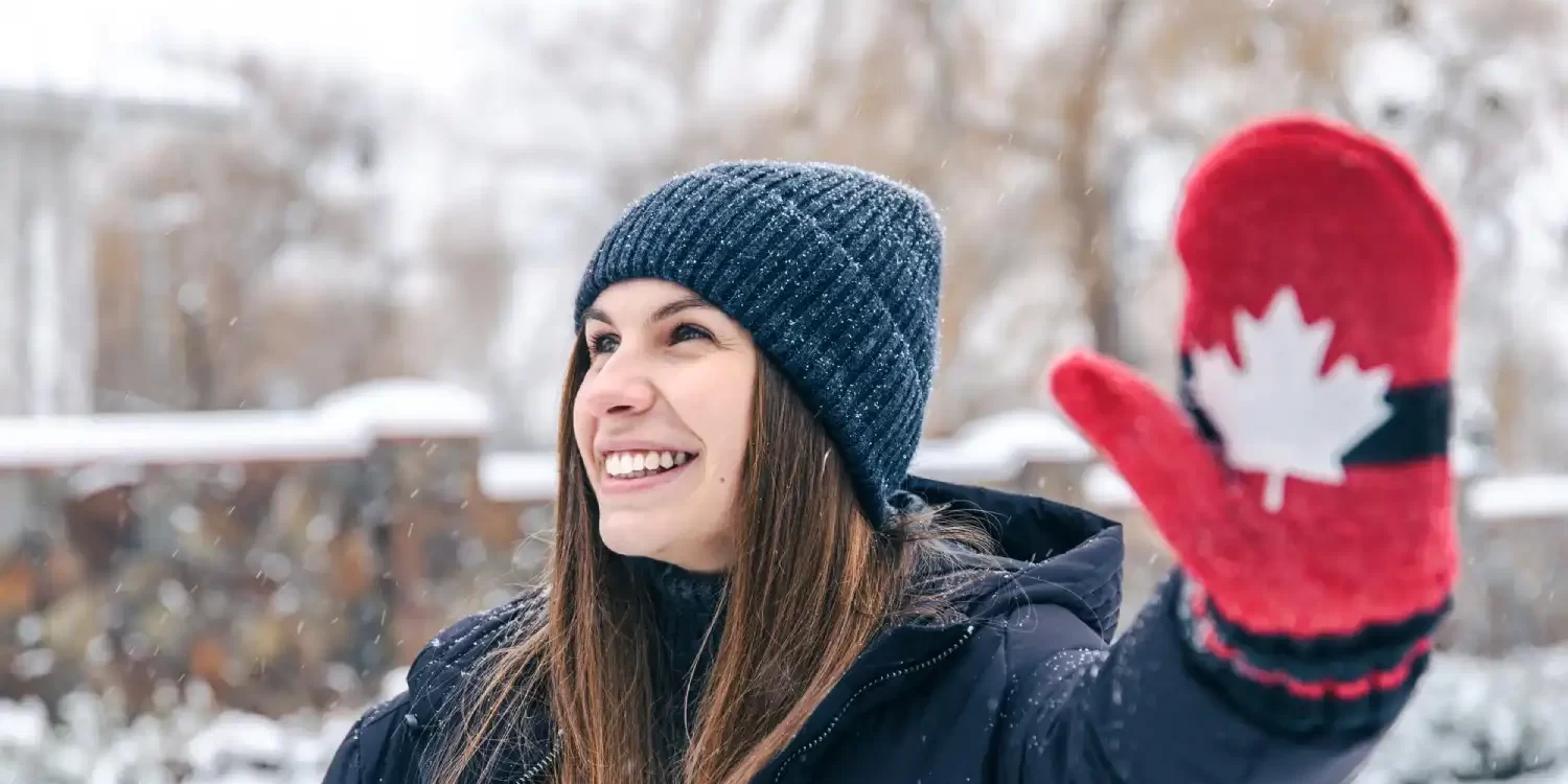 Happy young woman in red mittens with the flag of canada in snowy weather