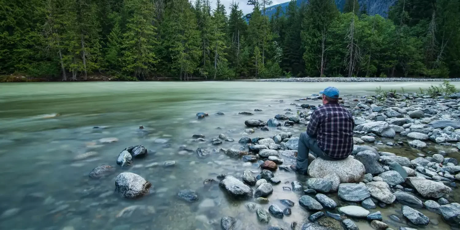 Person Sitting on Stone Near Body of Water