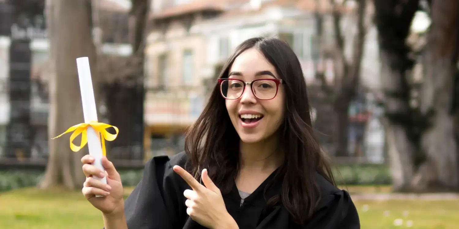 Young woman at graduation ceremony pointing to her diploma